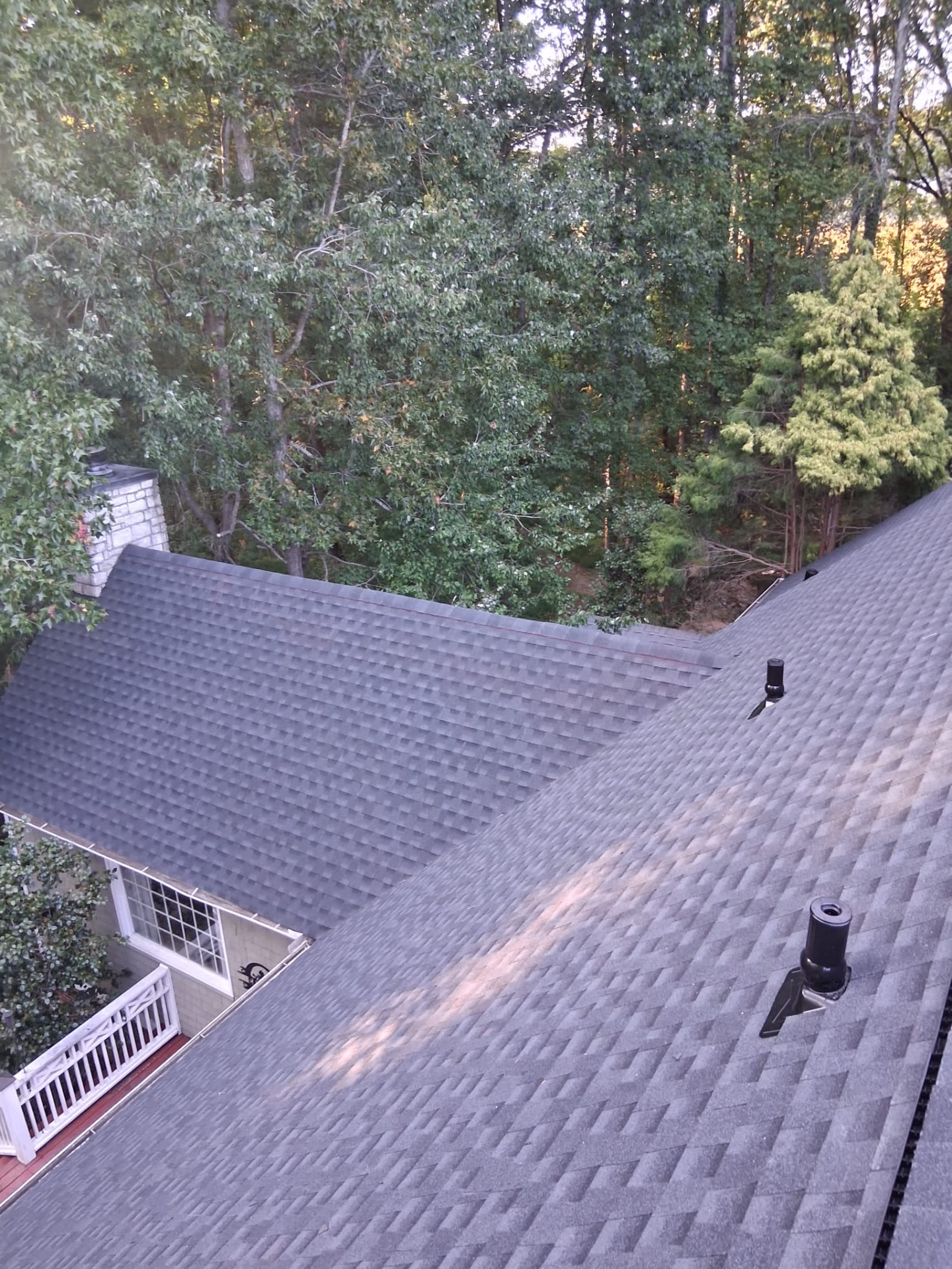 Aerial drone view of a dark charcoal architectural shingle roof with a stone chimney on a wooded lot
