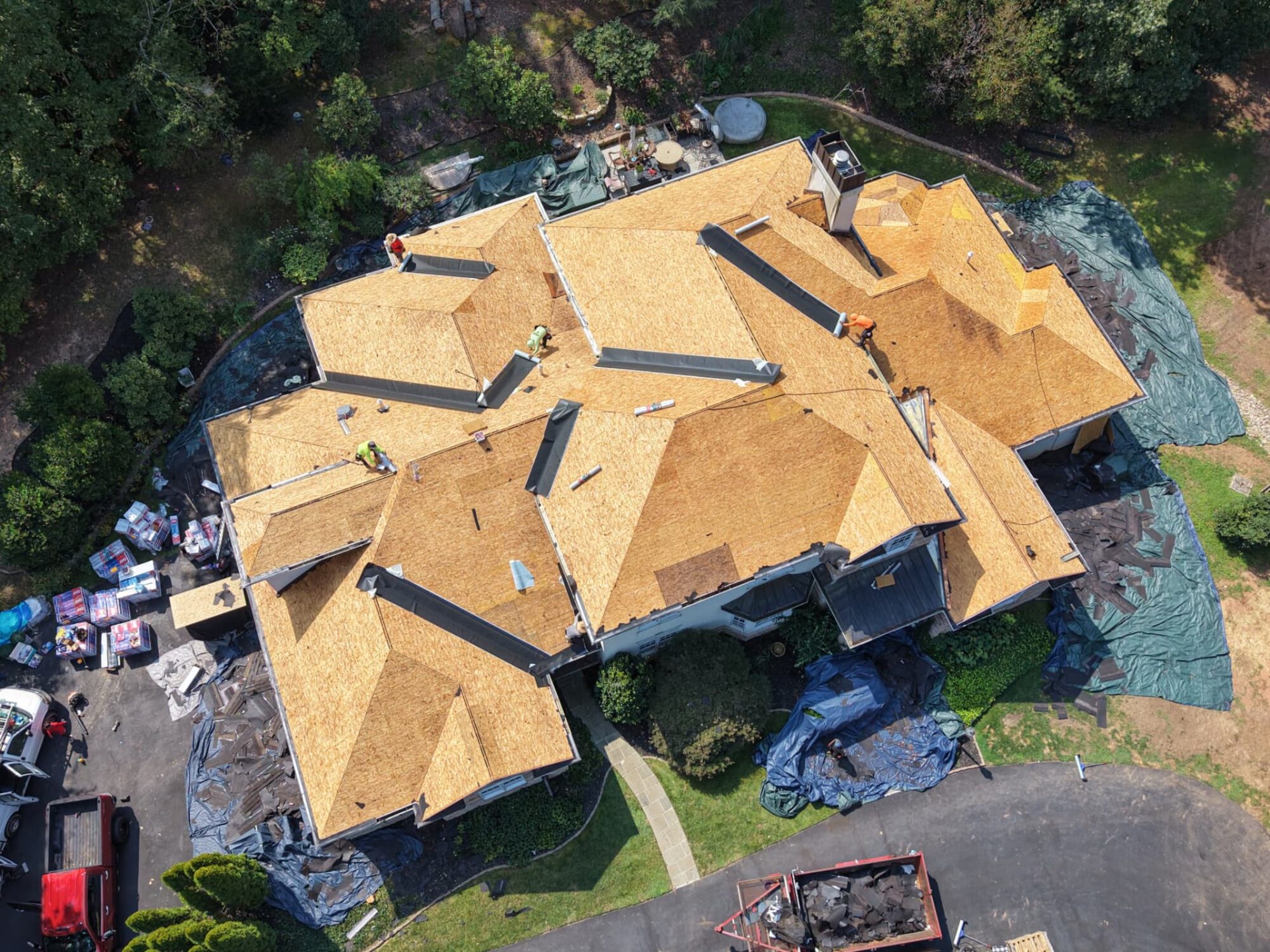 Aerial view of a large home stripped to fresh plywood decking with crew installing new underlayment