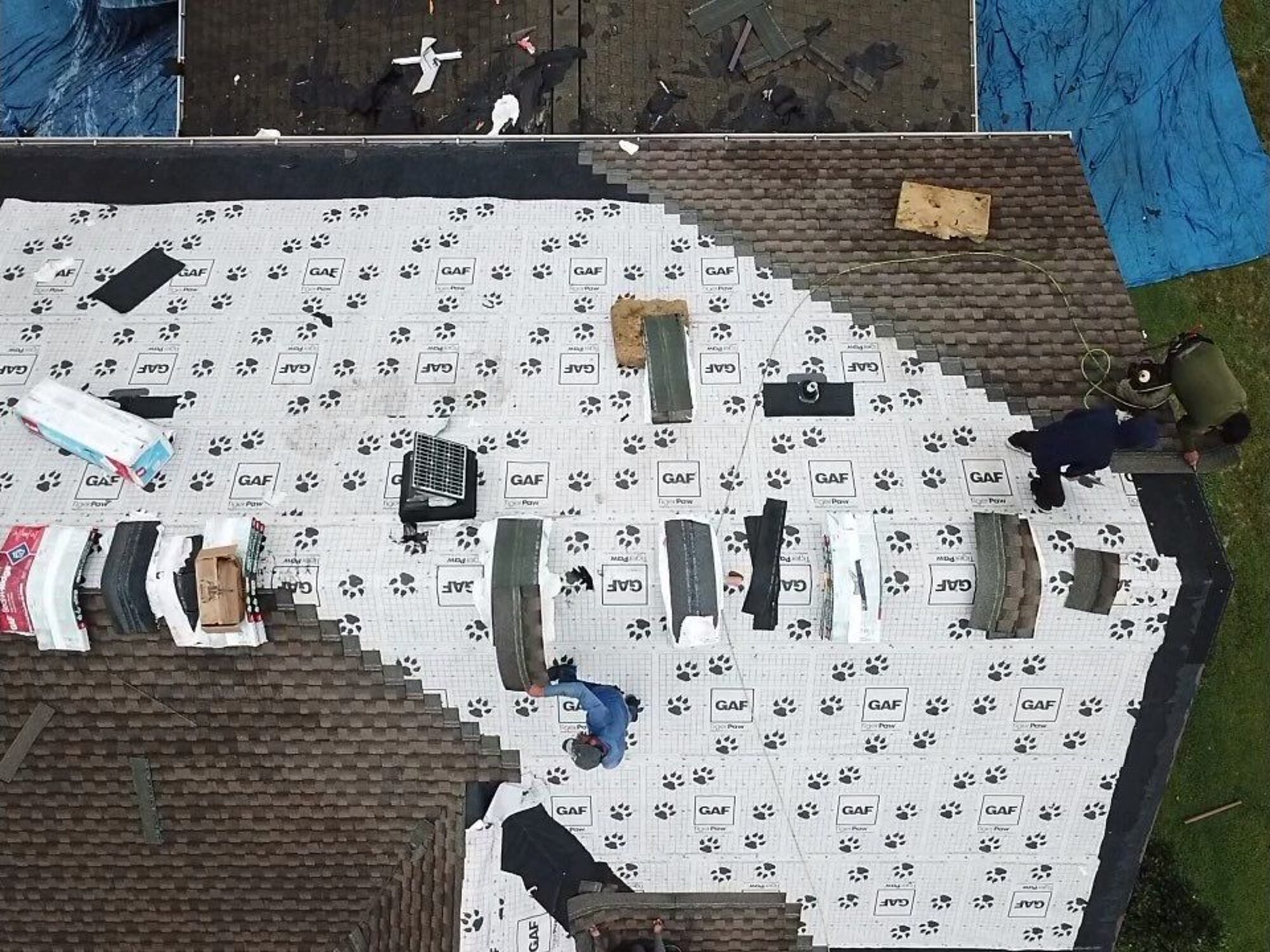 Overhead view of a roof half stripped with GAF underlayment installed and crew loading shingle bundles