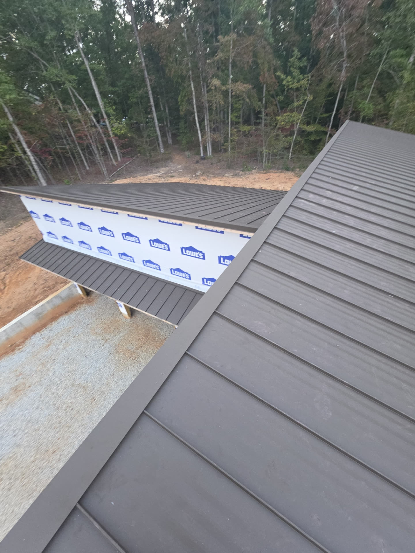 Aerial view of a new home wrapped in house wrap with a new dark bronze standing seam metal roof