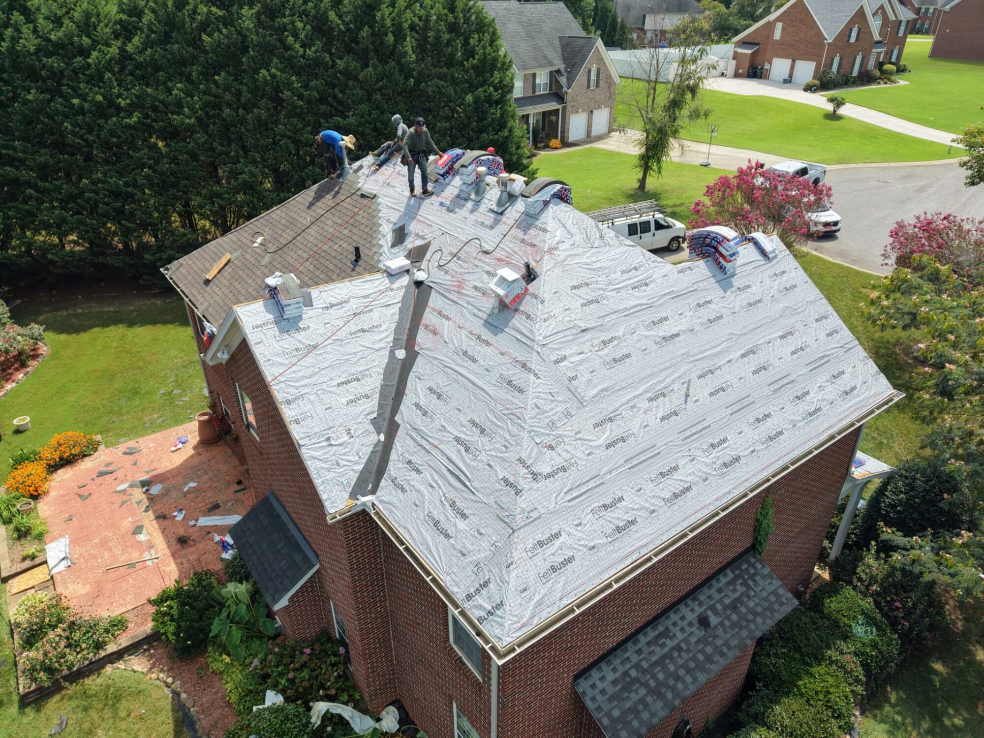 Two story brick home mid roof replacement with synthetic underlayment down and crew setting shingles at the ridge
