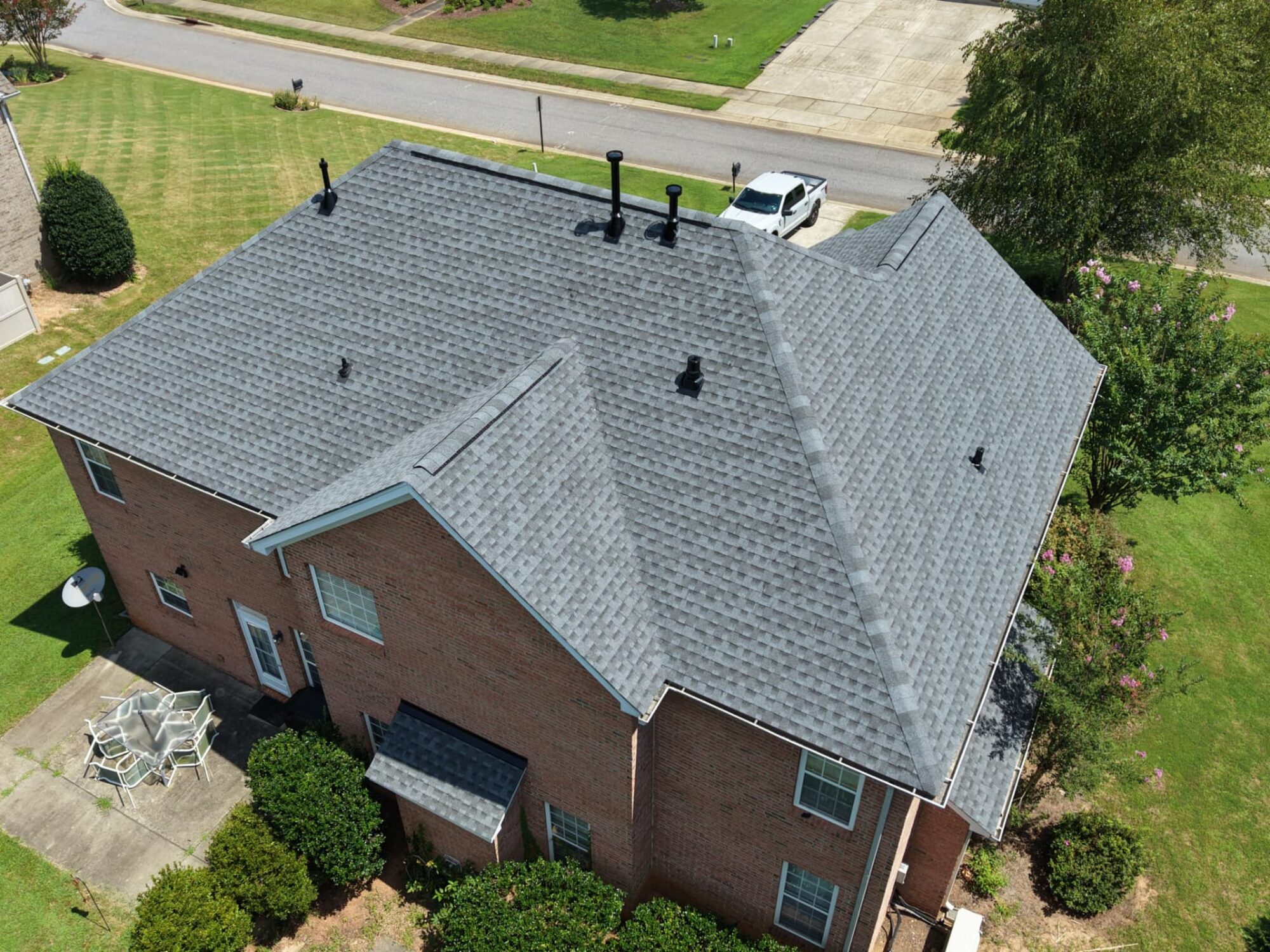 Two story brick home with a finished gray architectural shingle roof and new black vent boots
