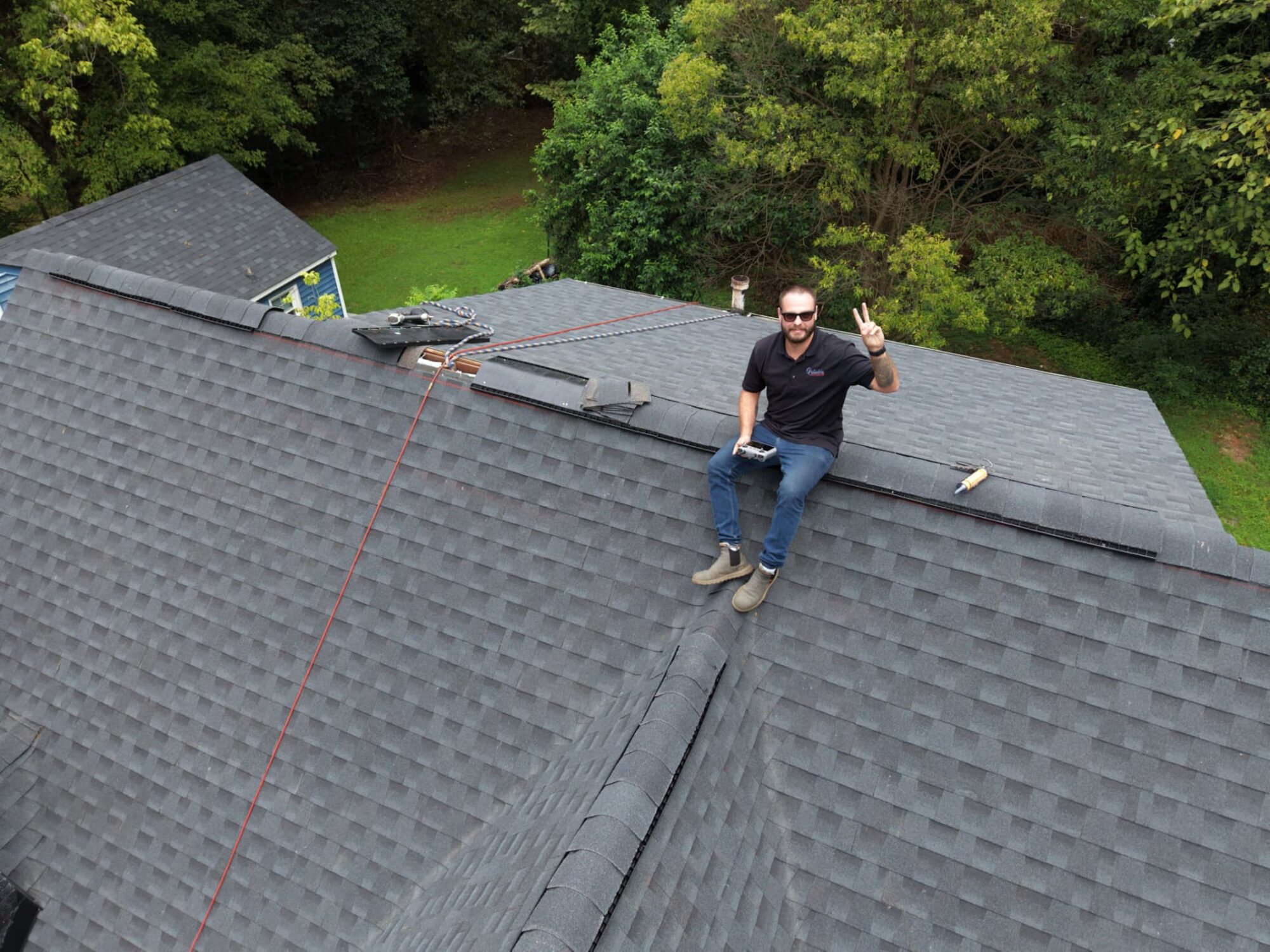 Reliable Roof and Gutter owner sitting on a finished charcoal shingle roof holding a drone controller